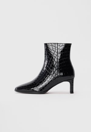 Bottine en cuir verni noir avec texture crocodile, bout pointu et talon slim de hauteur moyenne sur un fond blanc uni.