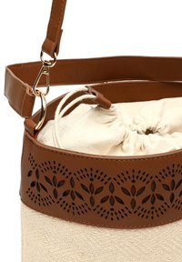 Sac à cordon en cuir brun avec des accents ; il présente un motif cousu sur le dessus et un corps en matériau naturel texturé. Sangle ajustable incluse.