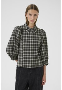 Cămașă cu carouri alb-negru, cu guler, mâneci bufante și croială lejeră, confecționată dintr-un material texturat. Purtați cu pantaloni din denim închis.