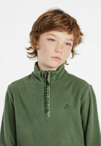 Pullover in pile verde con colletto alto e zip a metà, caratterizzato da una striscia logo verticale a contrasto e un piccolo logo ricamato sul petto.