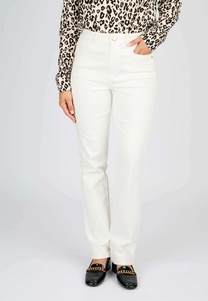 Pantalon taille haute blanc avec une jambe droite. Le tissu est lisse et comporte des poches avant. Associé à des mocassins noirs avec un accent en chaîne dorée.