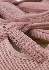 Dettaglio ravvicinato di una scarpa rosa, con texture, che presenta un laccio in rete e un bordo cucito, evidenziando i suoi elementi di design delicati e moderni.