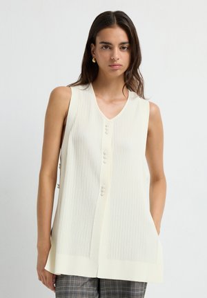 Lichtcreme mouwloze sweatervest met verticale ribbels, V-hals en een knoopsluiting aan de voorkant. Heeft een gestructureerde afwerking en zijsplitten.