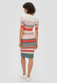 Robe en tricot avec des rayures horizontales rose, rouge, gris et vert. Manches courtes, coupe ajustée et texture côtelée à l'ourlet. Associée à des chaussures blanches.