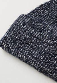 Beanie lavorato a maglia di colore blu navy con un motivo testurizzato. Il materiale presenta fibre metalliche, creando una lucentezza sottile. Design con risvolto.