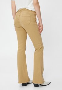 Eng anliegende, ausgestellte beiger Jeans mit mittelhoher Taille, zwei Gesäßtaschen und dezenten Nähdetails, kombiniert mit weißen spitzen Ankle Boots.