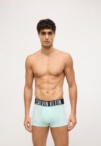 Mėtų žalios spalvos bokseriai su juodu Calvin Klein logotipo juosmeniu. Audinys atrodo minkštas ir tamprus, su prigludusia forma ir minimaliais akcentais.