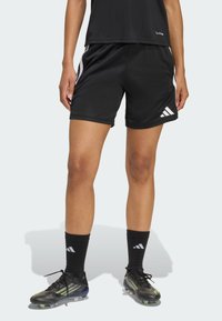 Μαύρο αθλητικό σορτς με λευκές λεπτομέρειες, κατασκευασμένο από λείο ύφασμα. Συνδυασμένο με μαύρες κάλτσες που έχουν λευκό λογότυπο και ποδοσφαιρικά παπούτσια με αγκράφες.