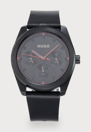 Black analog watch with a round case, featuring a dark dial, red accents, three sub-dials, and a black leather strap.