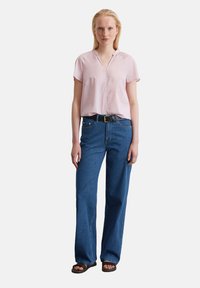 Helles rosa Kurzarmhemd mit V-Ausschnitt, kombiniert mit dunkelblauen weit geschnittenen Jeans und einem schwarzen Gürtel. Sandalen mit Riemen runden das Outfit ab.