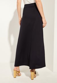 Svart maxikjol med en slät textur och hög midja, kombinerad med sandaler med guldblockhögda klackar. Designen har en flödande silhuett.