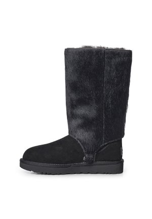 Bota de invierno negra hasta media pantorrilla con puntera de ante suave y caña con textura de piel, suela de goma plana y costuras visibles a los lados.