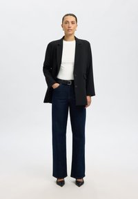 Črni blazer čez belo majico, združeno z visokim pasom in širokimi temno modrimi kavbojkami. Črni čevlji z ostrimi konicami zaokrožijo videz.