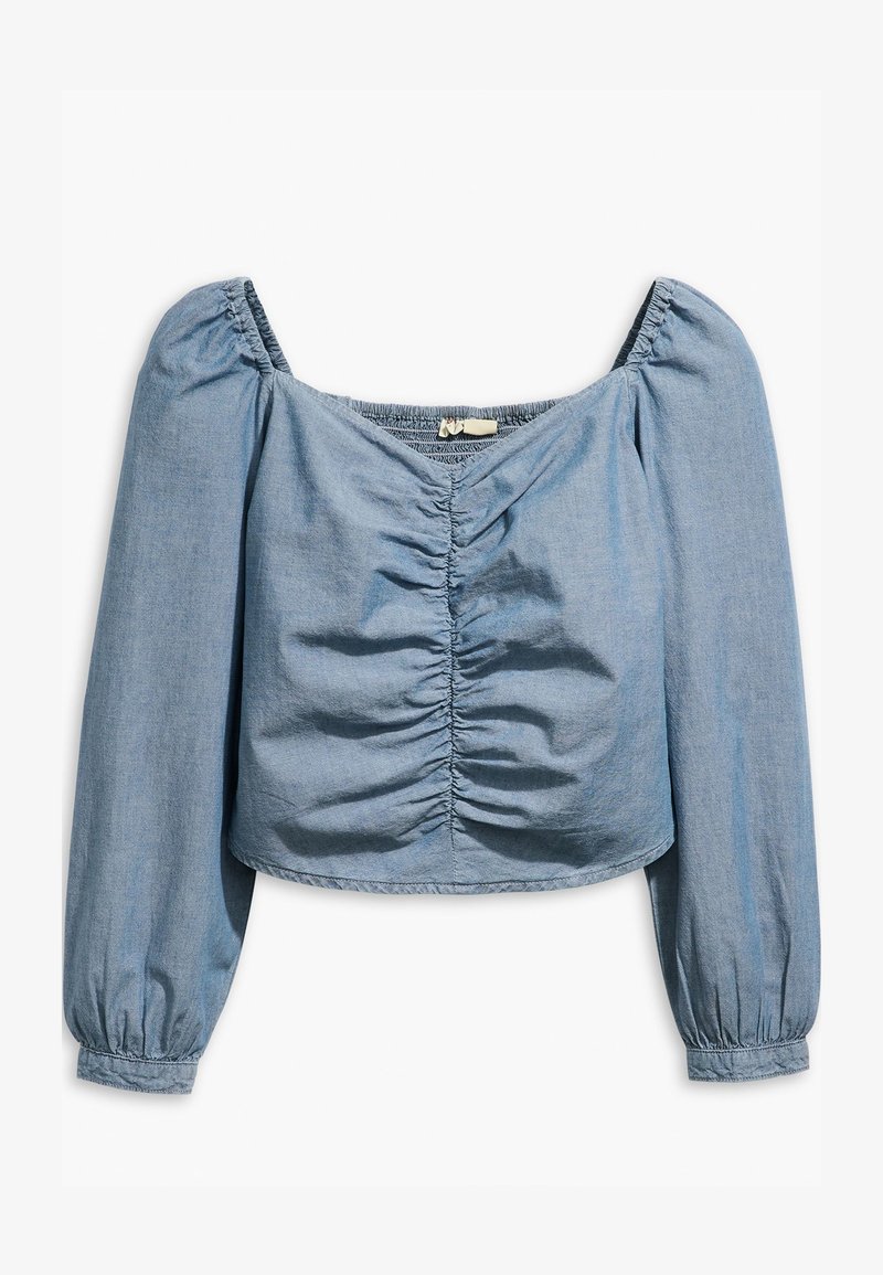Blouse bleu clair, à manches longues et coupée, en denim doux. Caractéristiques : tissu froncé à l'avant et encolure et poignets élastiqués.