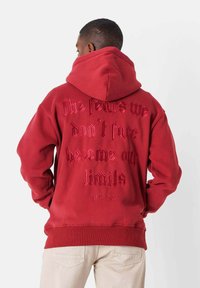 Sudadera roja con un gran estampado de texto en la parte posterior, que presenta un diseño bordado. Material de mezcla de algodón, puños y dobladillo acanalados.