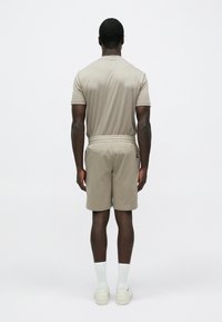 Bēša krāsas īsām piedurknēm krekls un tam saskaņotas bikses šorti, izgatavoti no mīksta auduma. Šorti ar elastīgu vidukļa jostu, attēloti no aizmugures.