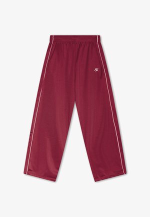 Calças desportivas vermelhas com riscas brancas laterais, cintura elástica e um pequeno "K" branco bordado na coxa direita.