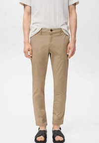 Pantaloni chino beige con vestibilità slim, realizzati in tessuto misto cotone. Presentano una chiusura con bottone e tasche laterali, abbinati a sandali neri.