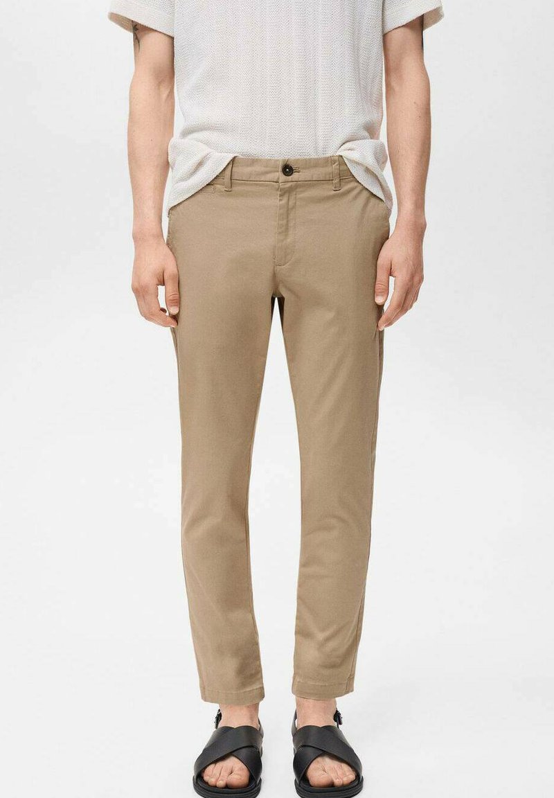 Pantaloni chino beige con vestibilità slim, realizzati in tessuto misto cotone. Presentano una chiusura con bottone e tasche laterali, abbinati a sandali neri.