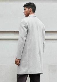 Abrigo de lana gris claro con corte recto, cuello de un solo botón y bolsillos laterales. Textura suave, diseño minimalista y sin patrones visibles.