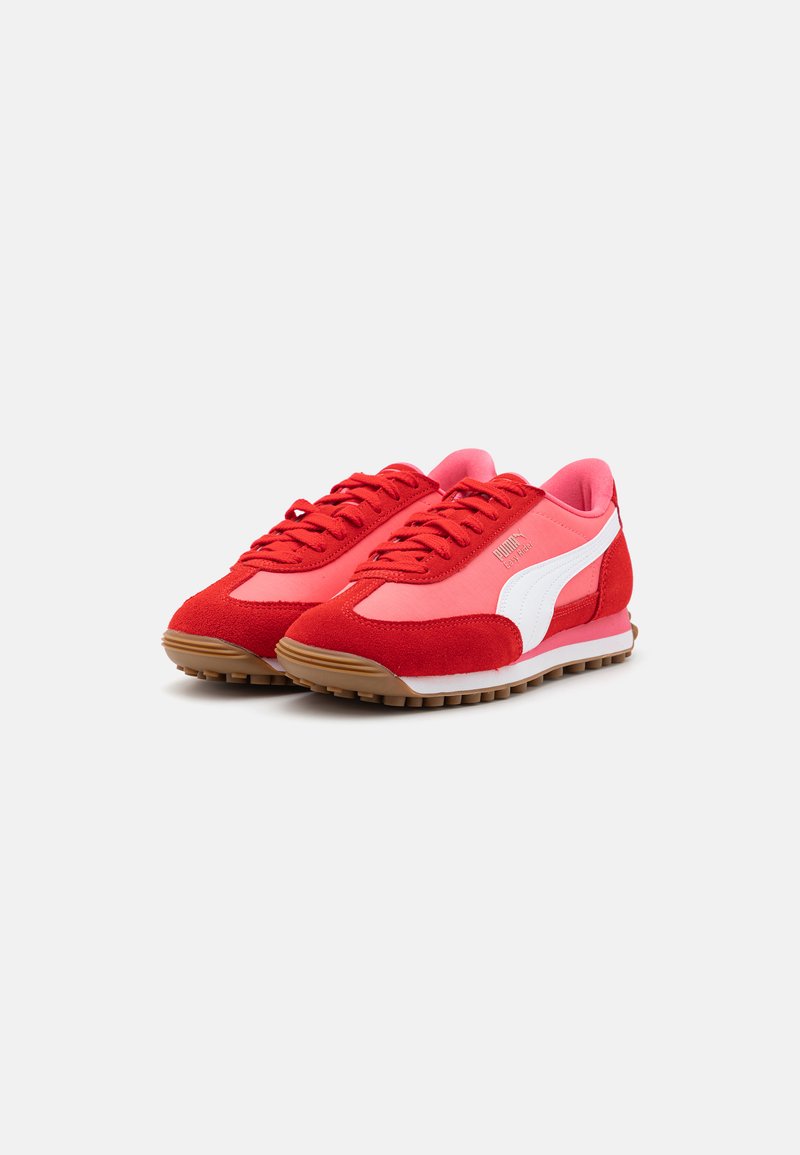 Chaussures de sport rouges avec des surfaces en suede et en mesh, présentant des accents blancs, des lacets ronds et une semelle en caoutchouc avec une texture adhérente.