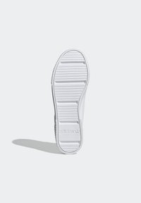 White sneaker outsole featuring horizontal grooves for traction and embossed logo detail. Smooth surface with rounded heel and toe sections.