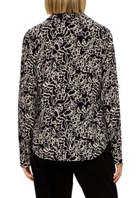 Blusa leggera a maniche lunghe nera con un motivo floreale astratto color crema, caratterizzata da un orlo curvo e un taglio morbido.