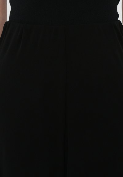 Schwarze Stoffhosen mit glatter Textur und elastischem Bund. Sie bieten eine lockere Passform mit dezenten Falten entlang der vorderen Naht.