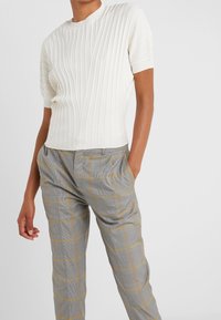 Top de punto blanco con relieve y manga corta, combinado con pantalones de cuadros grises con acentos amarillos y un corte relajado. Tejido texturizado y diseño estructurado.