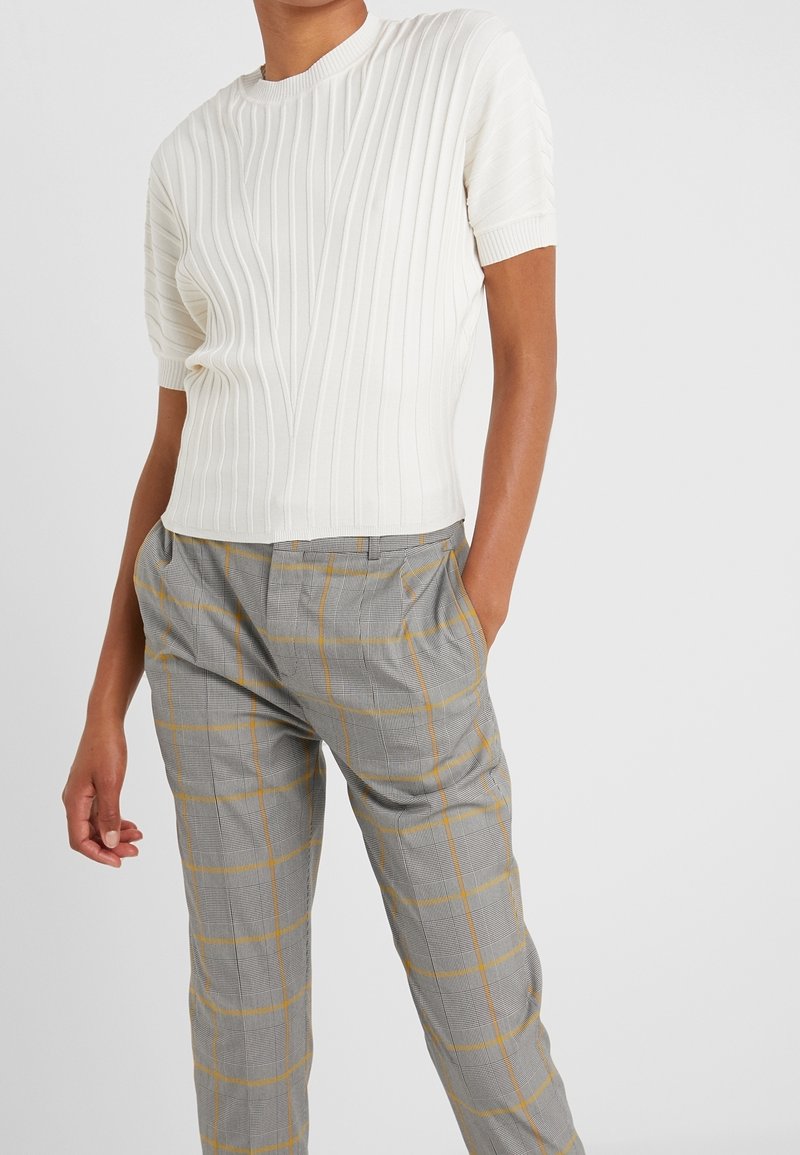 Top de punto blanco con relieve y manga corta, combinado con pantalones de cuadros grises con acentos amarillos y un corte relajado. Tejido texturizado y diseño estructurado.