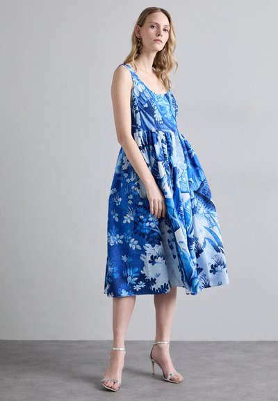Blue floral print dress featuring a flared skirt and thin straps, made of lightweight fabric. Paired with silver heeled sandals.