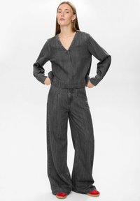 Completo a due pezzi di colore grigio scuro, simile al denim, con top a scollo a V, maniche lunghe e vita arricciata, abbinato a pantaloni a gamba larga. Calzature rosse.