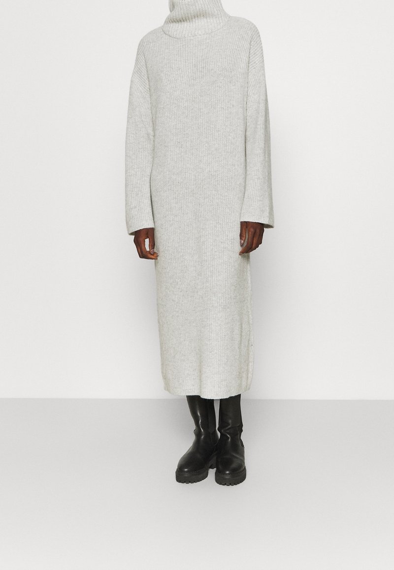 Vestito lungo grigio in maglia a coste con collo alto e maniche larghe, abbinato a stivali neri al ginocchio. Tessuto morbido con vestibilità rilassata.