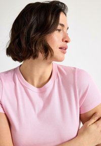 Maglietta rosa a coste con maniche corte e scollo rotondo. Il tessuto sembra morbido, con una leggera trama visibile sulla superficie.