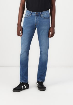 Jean en denim bleu avec une coupe droite, design à cinq poches et légères décolorations. Associés à des baskets noires avec des rayures blanches.