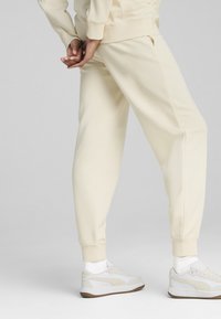 Crème-kleurige sweatpants met een relaxte pasvorm, voorzien van zijzakken en geribbelde boorden, gecombineerd met witte sneakers en crew-sokken.