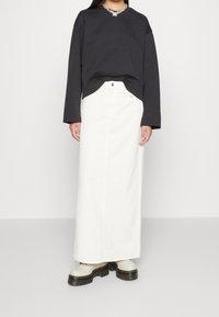 Mörkgrå sweatshirt med långa ärmar, kombinerad med en vit denim-maxikjol. Klumpiga stövlar i krämfärg med plattform. Enkelt utseende, inga mönster.