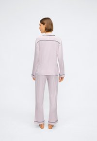 Set de pijamale de culoare mov deschis, realizat dintr-un material moale. Prezintă un top cu mâneci lungi, cu bordură neagră, și o pereche de pantaloni largi asortați.