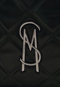 Surface en cuir matelassé noir avec un logo en métal argenté centré combinant les lettres S, M et A, gravé avec "Steve Madden."