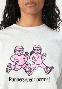 Grå hettegenser med en grafikk av to rosa tegneserie-løpere som har på seg capser og joggesko, med teksten "Løpere er ikke normale." under.