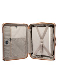 Valigia rigida con un guscio esterno beige, interno chiaro, tasche con zip e cinghie regolabili per fissare gli oggetti. Rivestimento interno a motivi visibile.