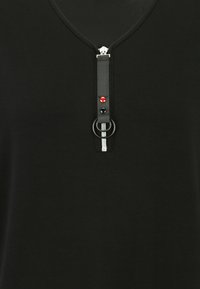 Schwarzes Kleidungsstück mit V-Ausschnitt und metallischem Reißverschluss. Es verfügt über einen texturierten Riemen mit roten und schwarzen Akzenten sowie einem kreisförmigen Ringdetail.