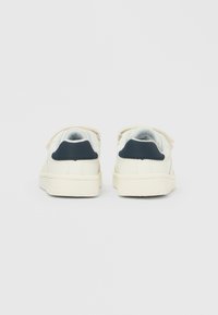 Coppia di scarpe da ginnastica bianche per bambini con inserti sul tallone di colore blu scuro, viste da dietro su uno sfondo semplice.