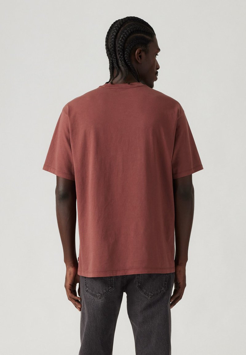 Camiseta de algodón color óxido con mangas cortas, cuello redondo y un corte holgado. La parte posterior presenta una textura suave y sin logotipos visibles.