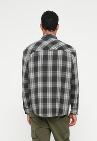 Juodai baltas languotas flanelinis marškinis su ilgomis rankovėmis, turintis išplėstą apykaklę ir apvalų galą, rodomas iš nugaros.