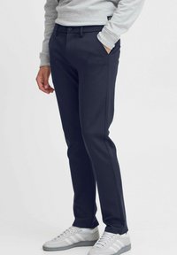 Pantalones azul marino con un diseño de pierna recta, que cuentan con una cinturilla abotonada, bolsillos laterales y una textura suave, combinados con zapatillas grises.