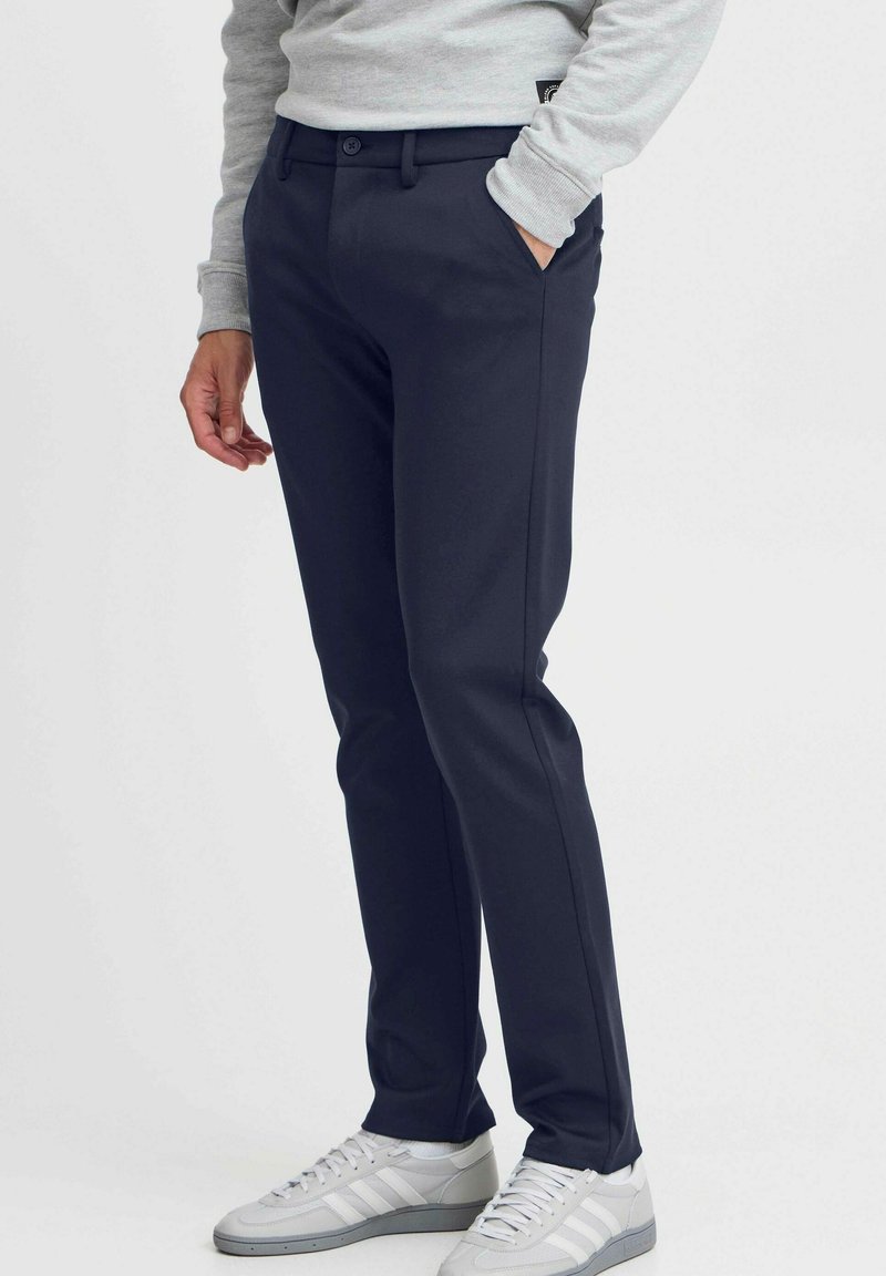 Pantalones azul marino con un diseño de pierna recta, que cuentan con una cinturilla abotonada, bolsillos laterales y una textura suave, combinados con zapatillas grises.