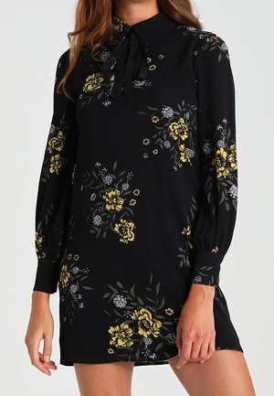 Long-sleeve black dress with yellow and white floral patterns, a tied bow at the collar, and cuffed sleeves.
