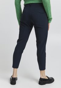 Marynarka w kolorze granatowym o dopasowanym kroju, z średnim stanem, zwężanymi nogawkami i minimalnymi kieszeniami z tyłu. Połączona z czarnymi butami na grubej podeszwie.