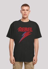 Black cotton t-shirt featuring bold red "REBEL" text and a red and blue lightning bolt graphic. Relaxed fit with short sleeves.